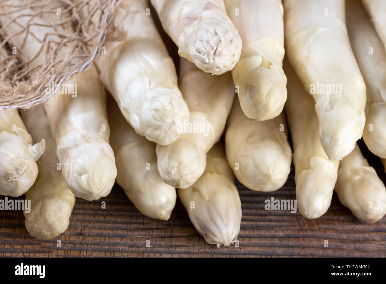 Close-up of the heads of a bunch of white asparagus spears on a rustic board Stock Photo