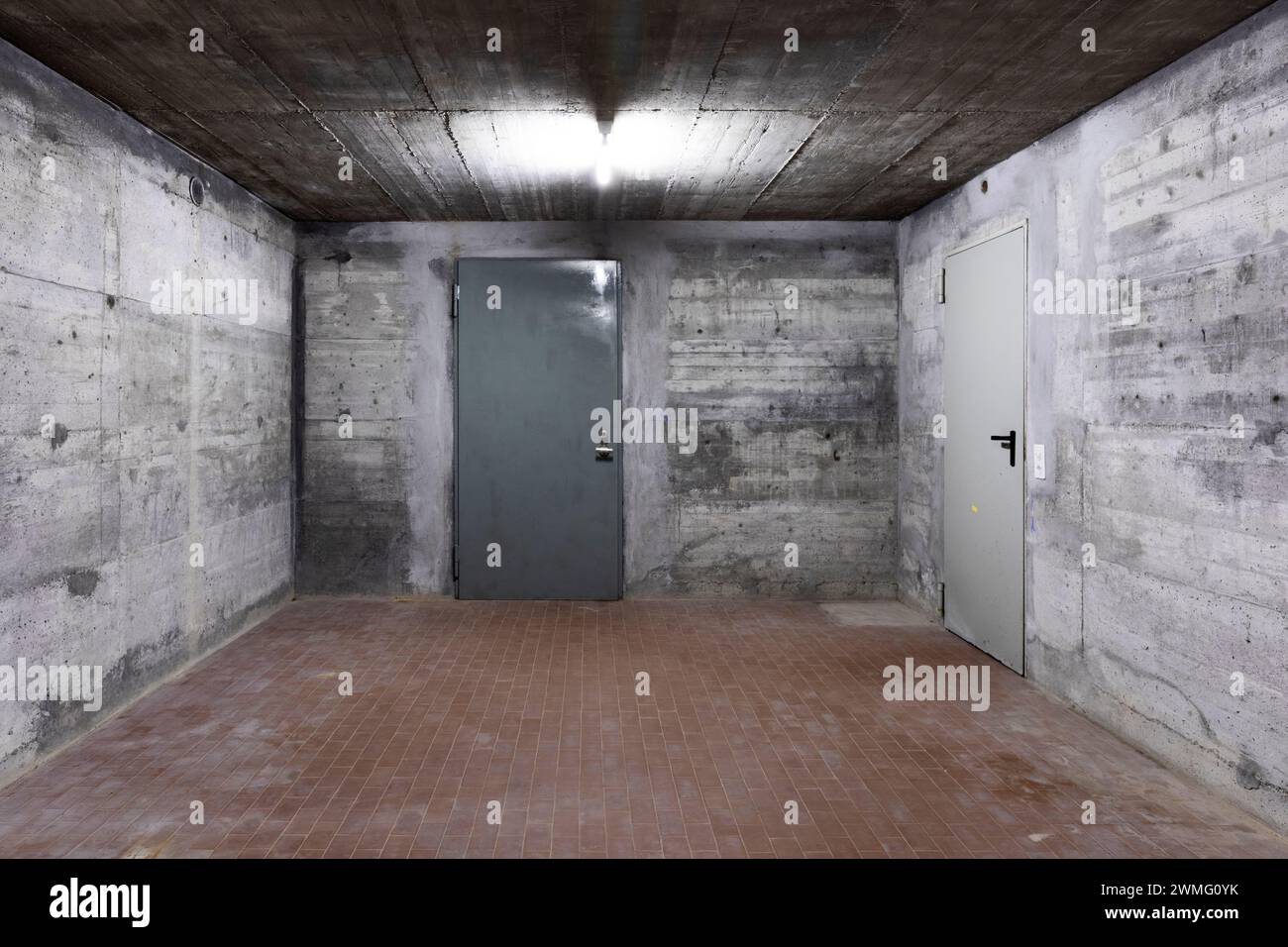 Front view of reinforced concrete wall of a bunker with closed armored door. Scene illuminated by a white neon lamp. Nobody inside Stock Photo