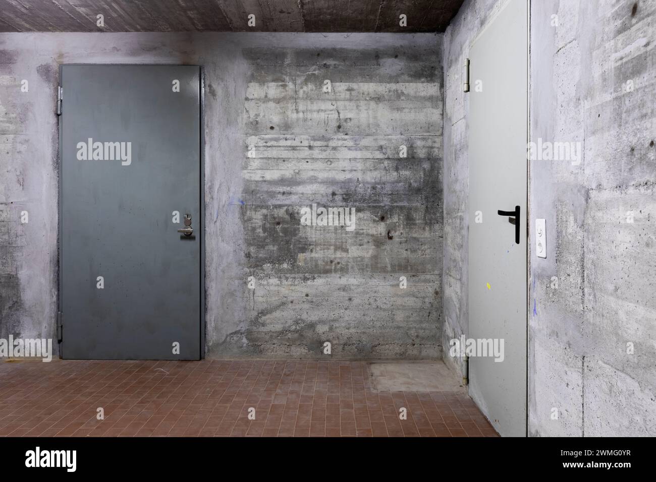 Front view of reinforced concrete wall of a bunker with closed armored door. Scene illuminated by a white neon lamp. Nobody inside Stock Photo