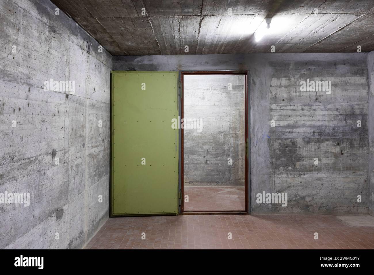 Front view of reinforced concrete wall of a bunker with open vault armored door. Scene illuminated by a white neon lamp. Nobody inside Stock Photo