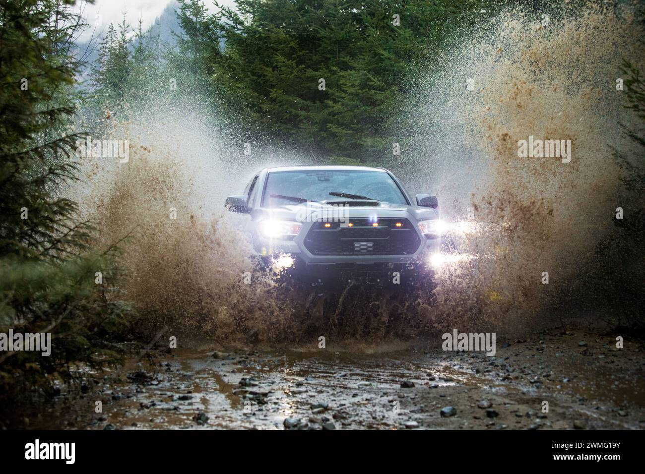 Truck with lights on powerfully drives through a flooded gravel road Stock Photo