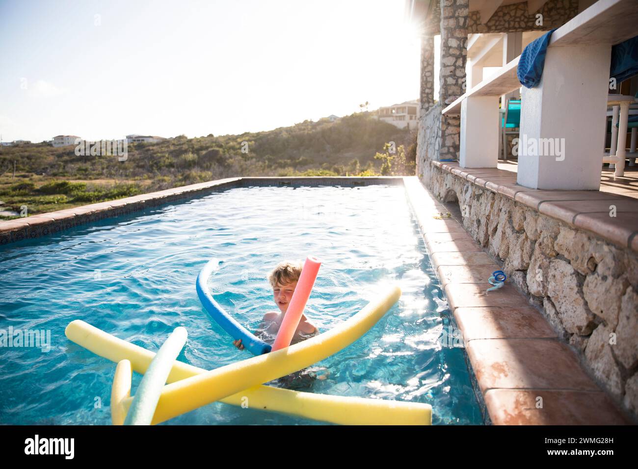 Young Boy With Pool Noodles, in Pool Overlooking Caribbean Beach Stock Photo