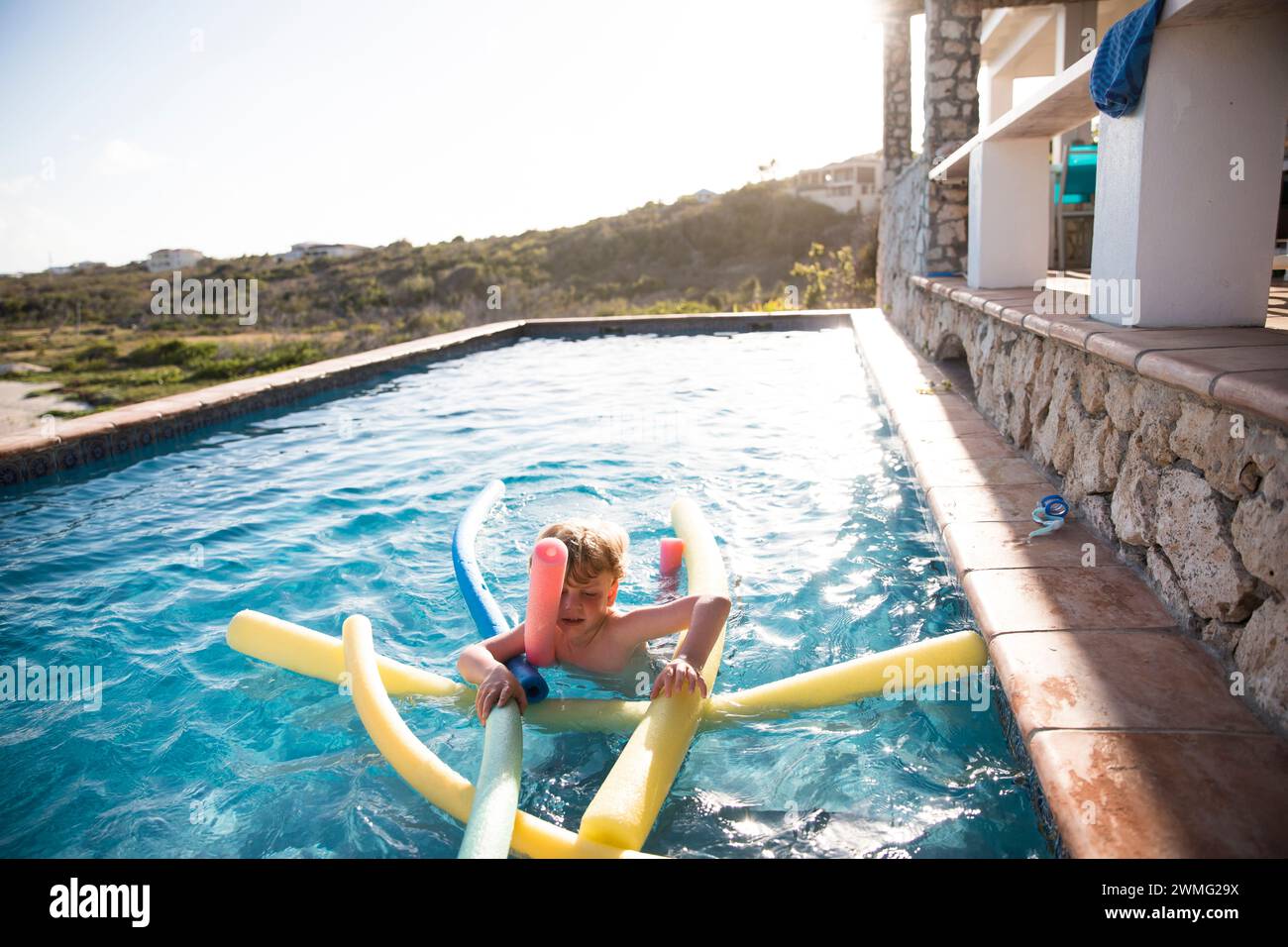 Young Boy Swims With Pool Noodles in Infinity Pool Stock Photo