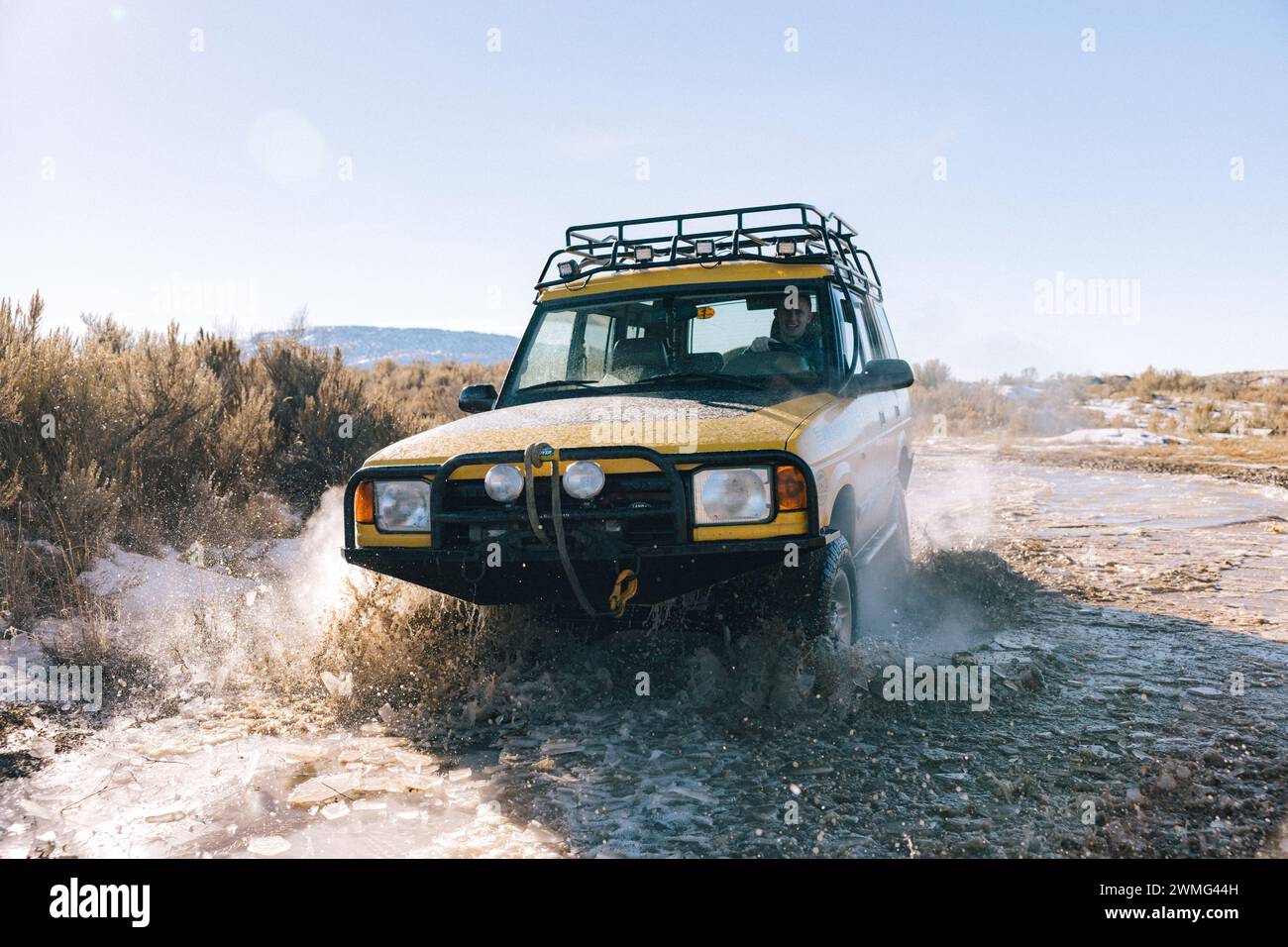 A backlit SUV drives through a puddle in the mountains. Stock Photo