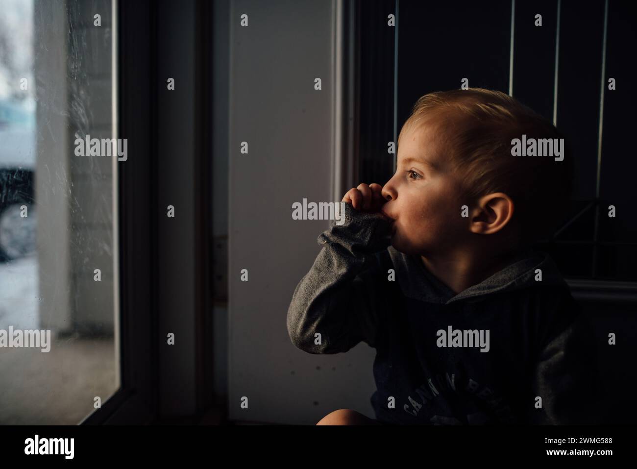 Profile of toddler sucking thumb while looking out window. Stock Photo