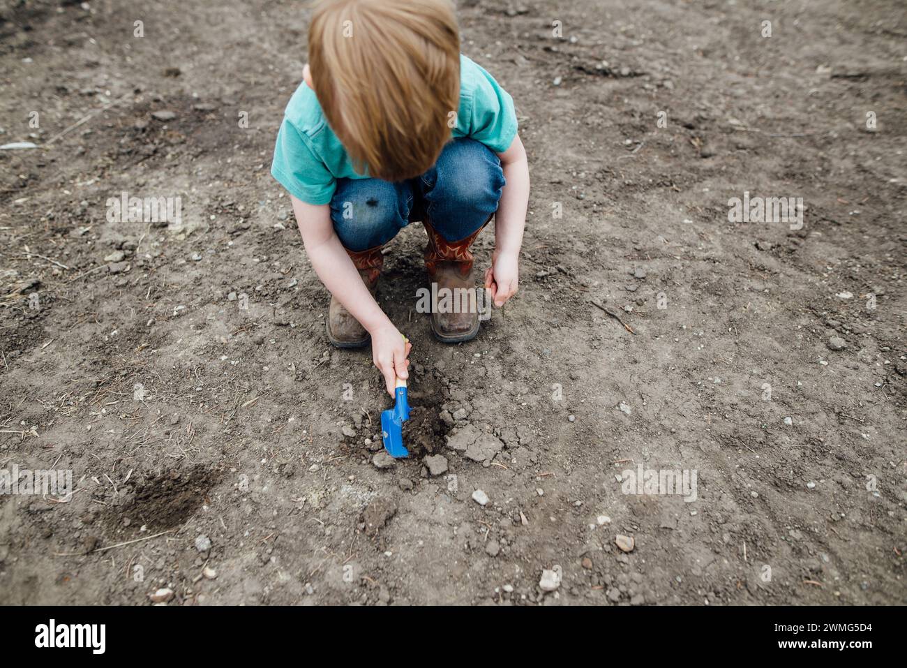 Overhead view of young boy squatting in dirt yard using a shovel Stock Photo