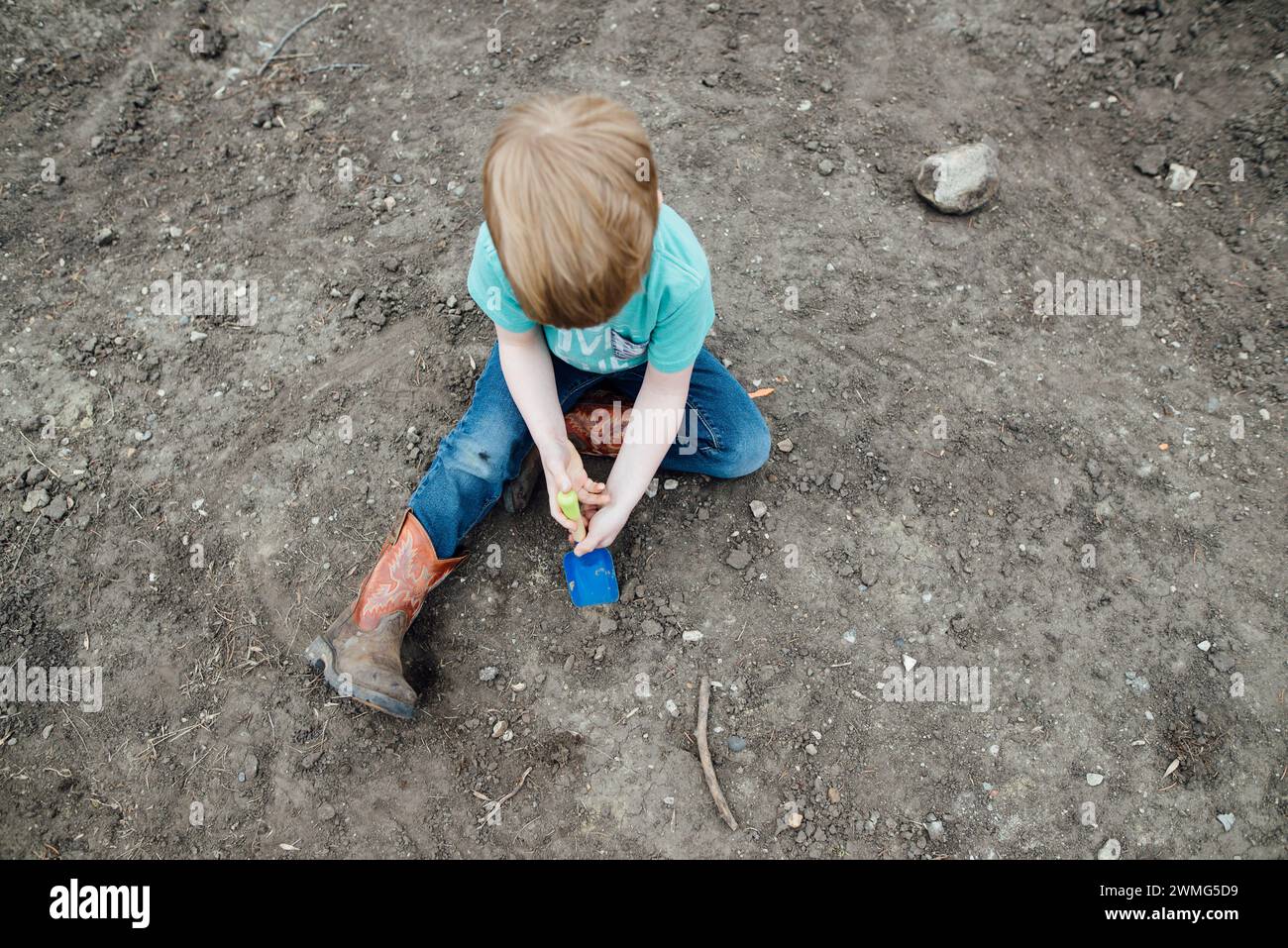 Overhead view of young boy sitting in dirt using a small shovel Stock Photo