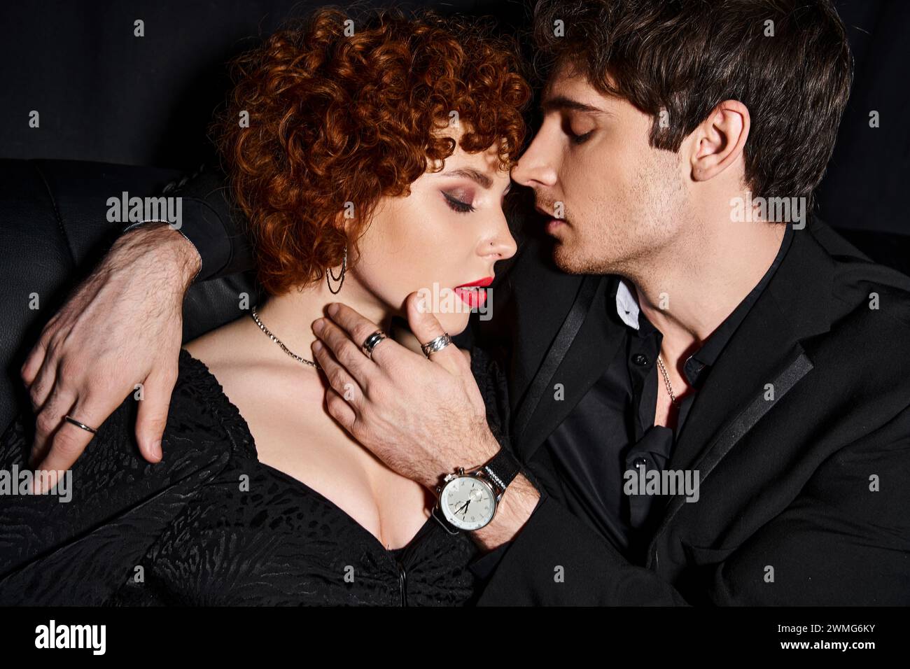 engaging boyfriend and girlfriend in elegant clothes hugging lovingly on  black sofa, sexy couple Stock Photo