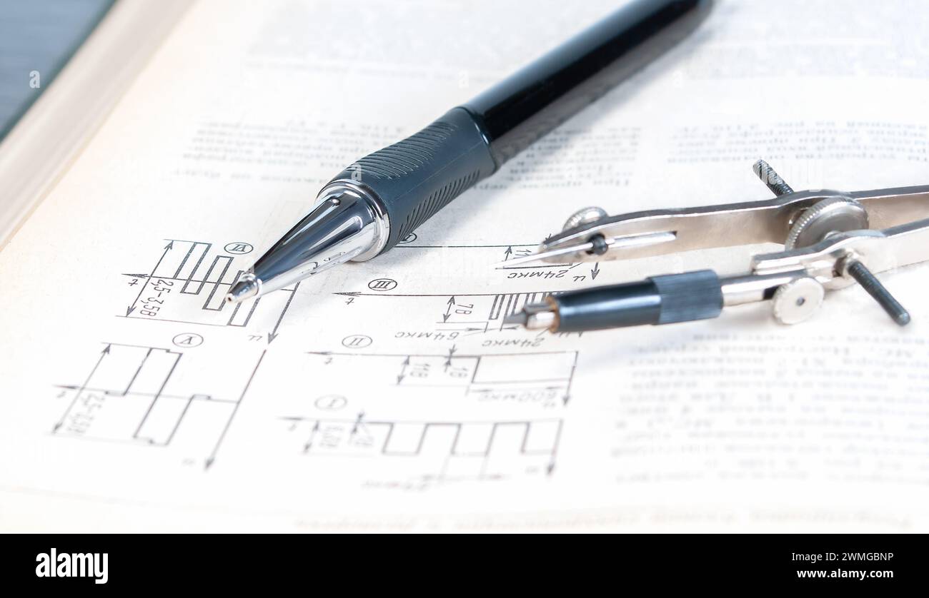 The pencil and circlet are on an open page of a technical reference book with electrical diagrams close up. Stock Photo