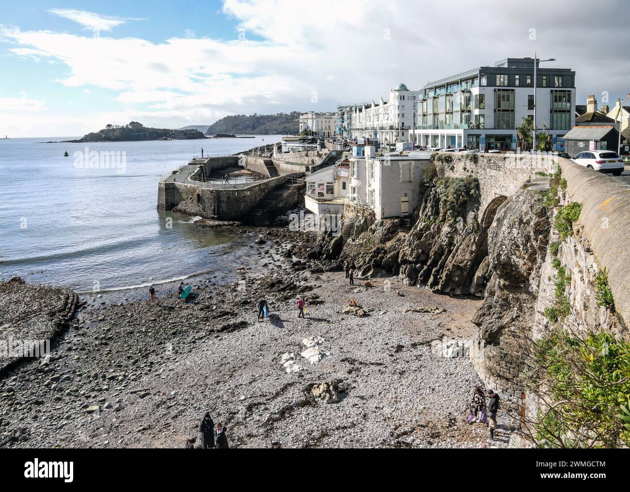 Paddle boarders enjoy late February sunshine on a pebble beach at West Hoe in Plymouth. The beach recently made safe from a dangerous cliff is free an Stock Photo