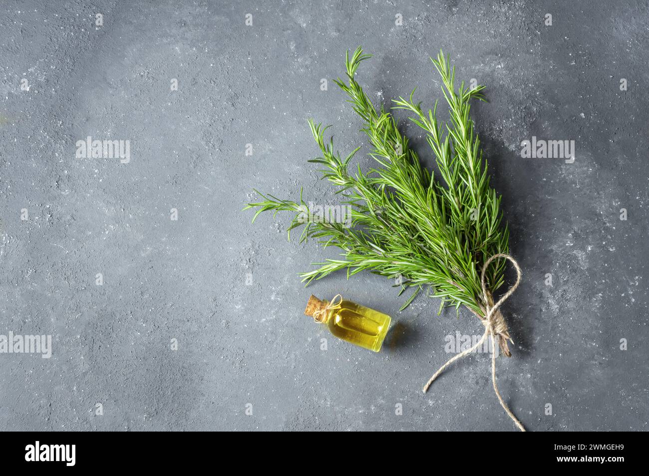 Glass bottle of essential rosemary oil with rosemary branch on rustic background. herbal oil concept, Rosmarinus Officinalis Stock Photo