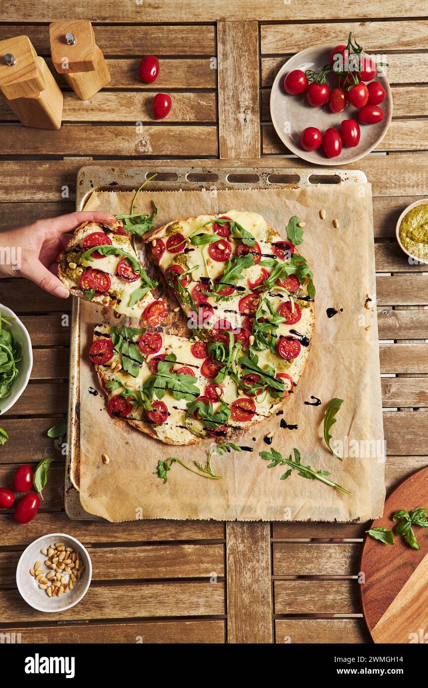 A freshly baked delicious pizza with tomato-mozzarella and arugula on a wooden table Stock Photo