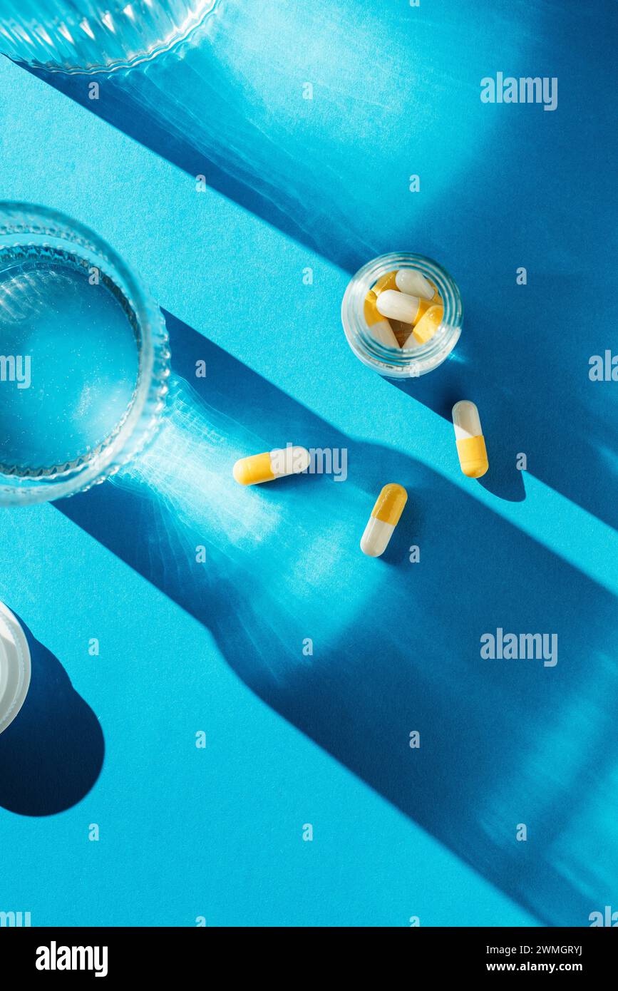 White and yellow capsule medicine on blue background with long shadows under direct sun light Stock Photo