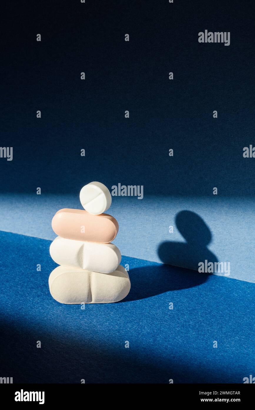 Stack of pills on blue background under direct light with long shadows Stock Photo
