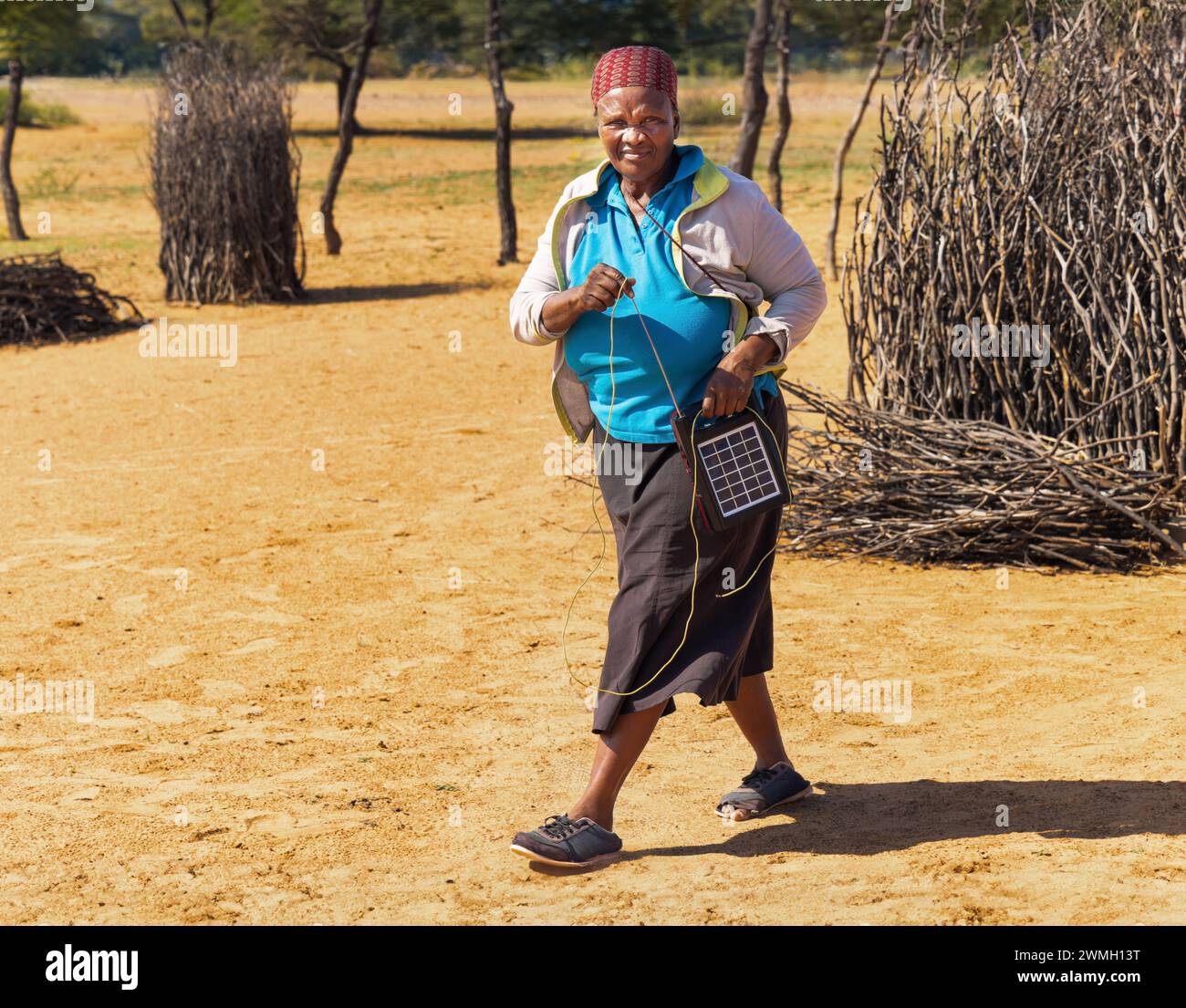 village old african woman using a solar panel with radio, to recharge phones and light, donated by a charity NGO, to improve life in rural areas Stock Photo