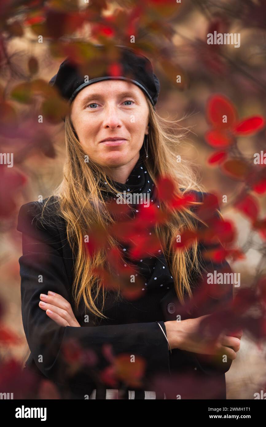 Chic Happy Young adult woman in a beret smiling framed and against a background of autumn greenery Stock Photo
