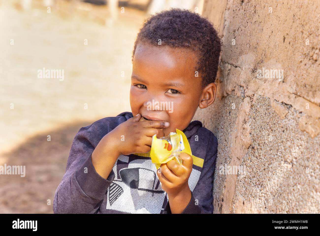 village african hungry child eating biscuits in the yard in a sunny day Stock Photo