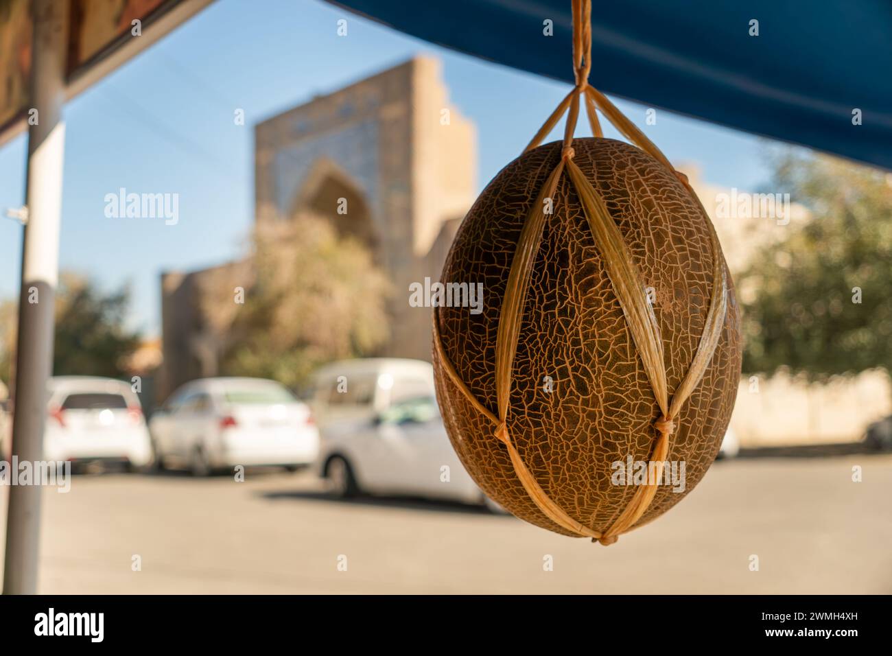 A ripe orange melon hangs on a rope against the background of a beautiful madrasah Stock Photo