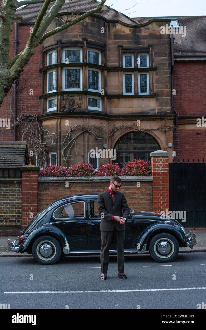 Young man arrive in style wearing a suit in fron of vintage black volkswagen beetle. Stock Photo