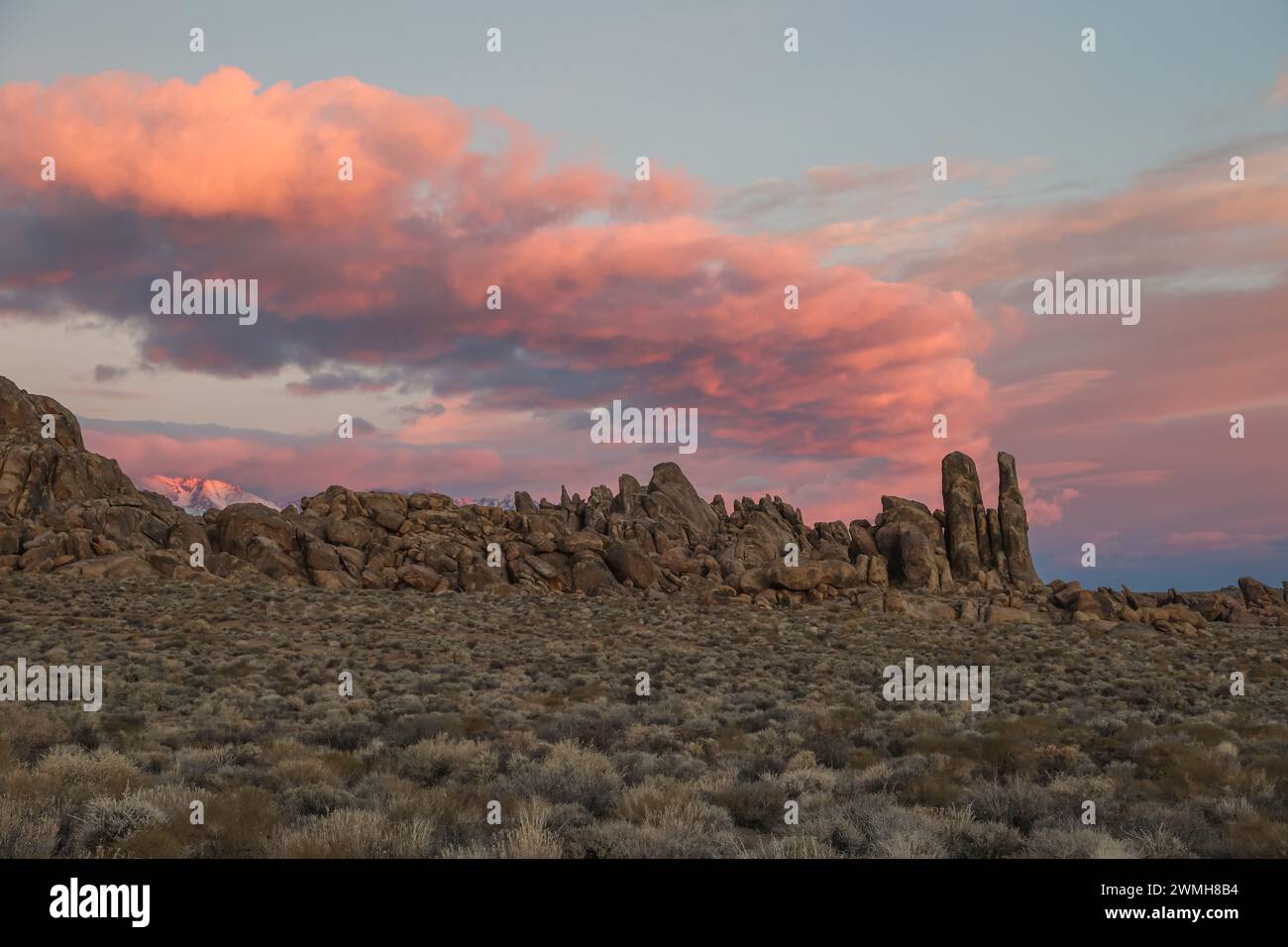 A colorful sunrise sky hovers in dramatic fashion above a complex rock and boulder feature in California's Alabama Hills. Stock Photo