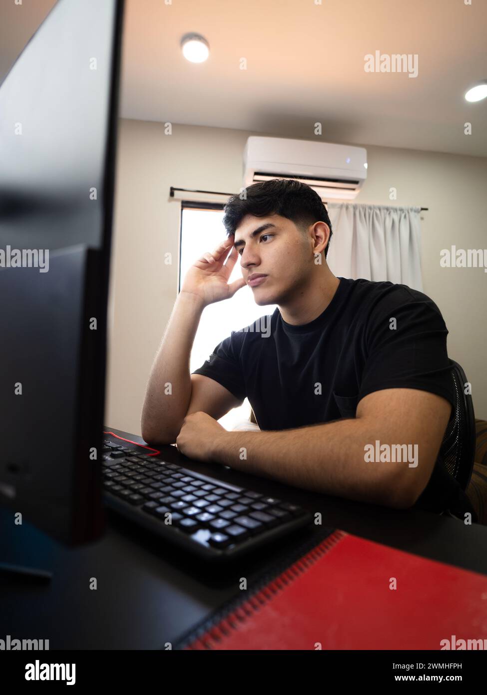 Vertical image of a youth immerses himself in school or work tasks in his living room, facing daily challenges with a reflective approach Stock Photo