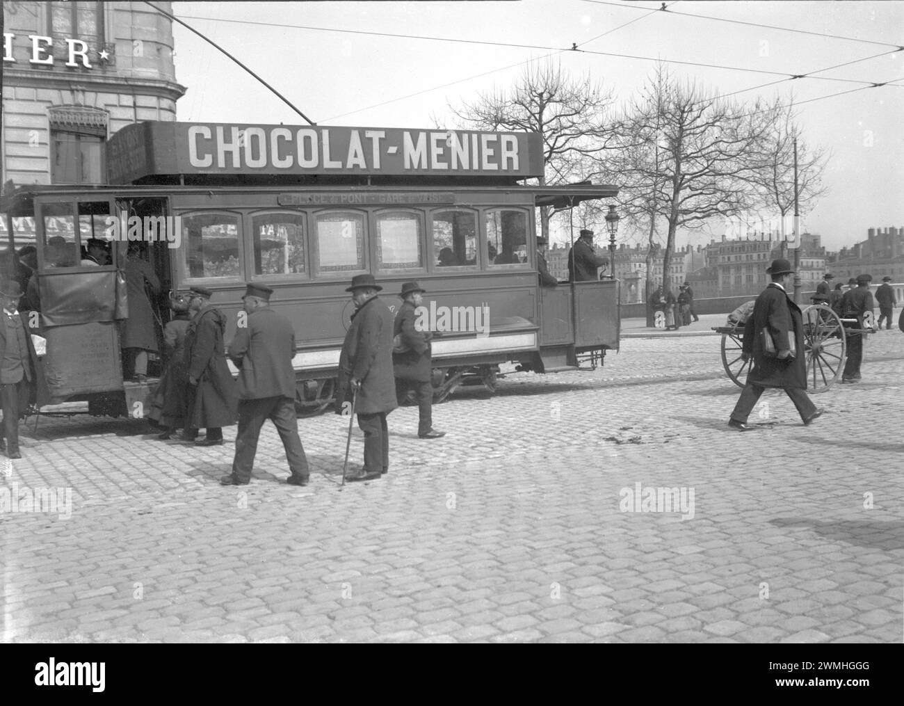 People walking in a paved street in Lyon. Next to a tramway with publicities. Beginning of 20th century. Old photograph digitized from glass plate Stock Photo