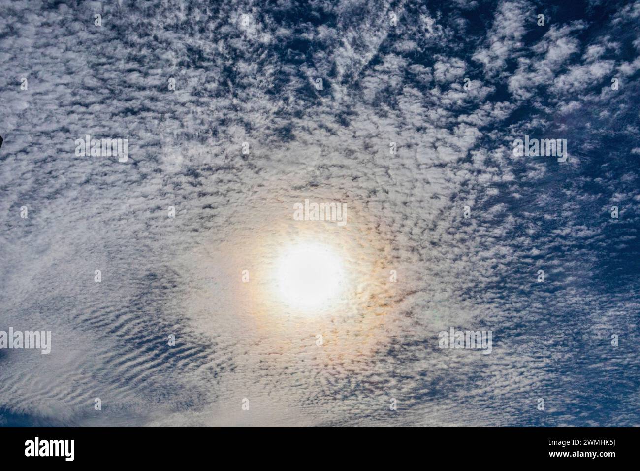 Looking at the sun through a layer of cirrocumulus stratiformis or altocumulus clouds. Stock Photo