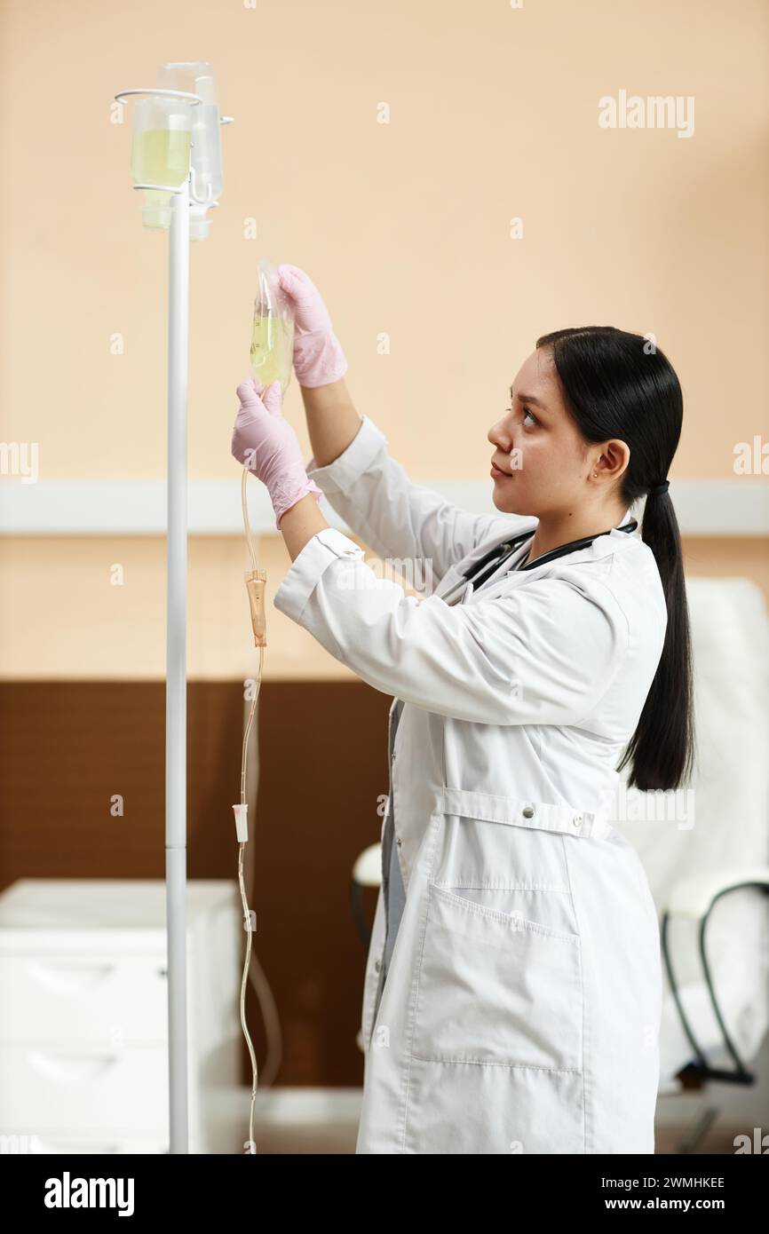 Vertical portrait of female doctor setting up equipment for IV drip treatment in procedure room Stock Photo