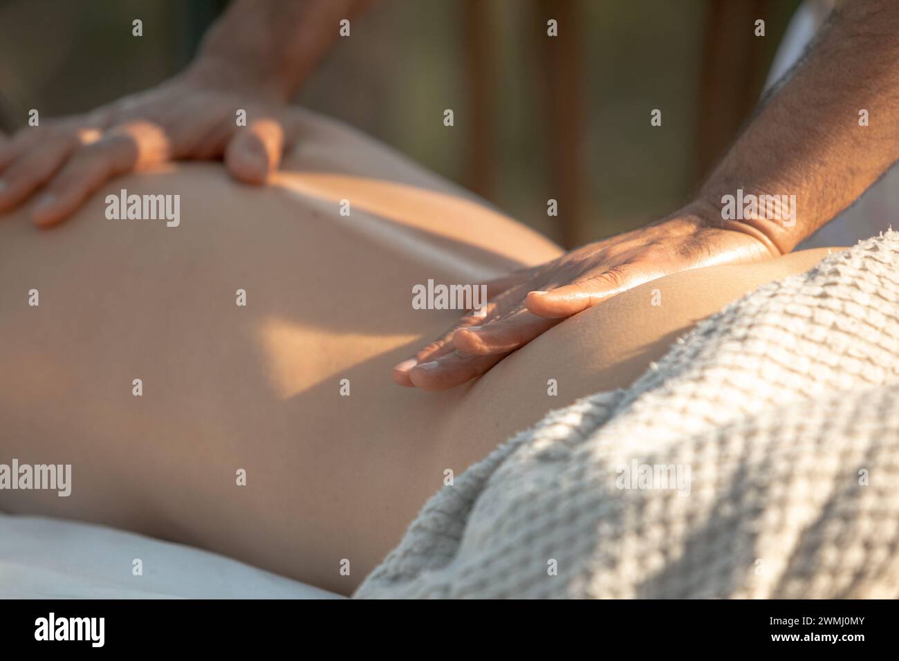Soothing Back Massage Therapy: Gentle Hand Strokes by a Professional on Female Client's Lower Back with Warm Sunset Light Stock Photo