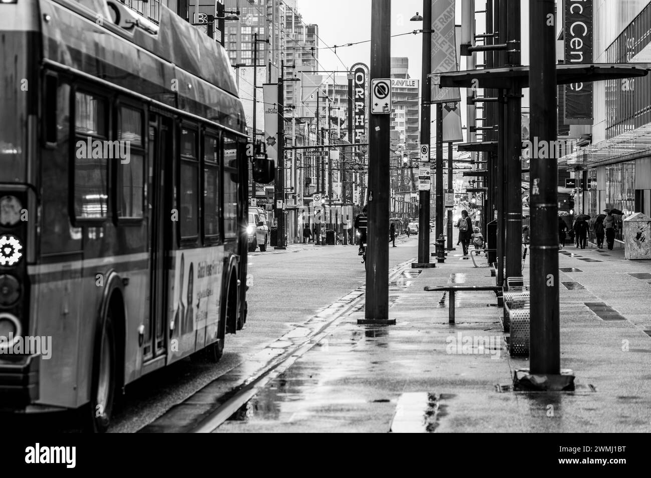 A black and white photo of a TransLink bus going down Granville street on a rainy day with people walking on the sidewalk holding umbrellas. Stock Photo