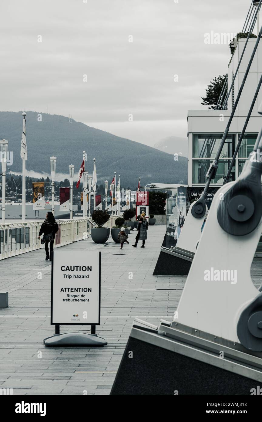 A view of the Canada Place pier walkway on an overcast day, with a child jumping playfully in front of a woman. Stock Photo