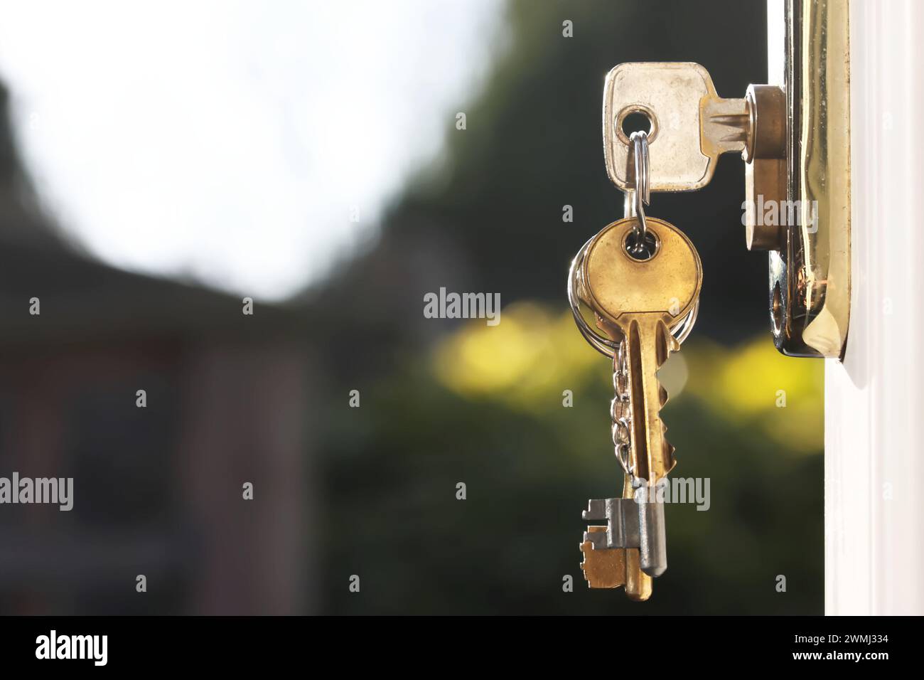 House keys in lock of a door viewed outside with soft glow background from natural lighting. Room for text Stock Photo