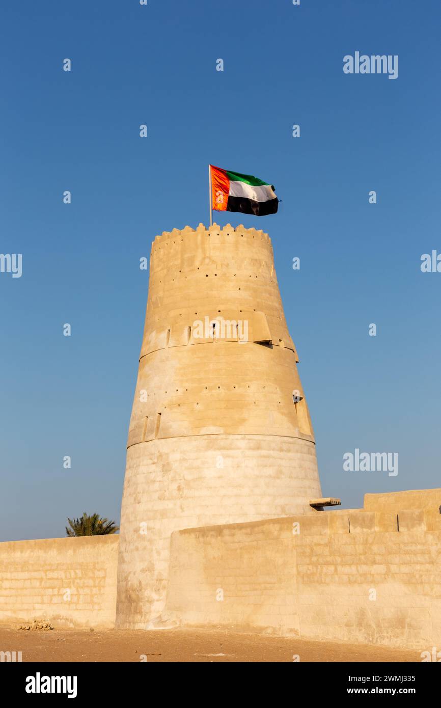 Stone arabic watchtower with waving United Arab Emirates National Flag in Al Jazirah Al Hamra haunted town in Ras Al Khaimah. Stock Photo
