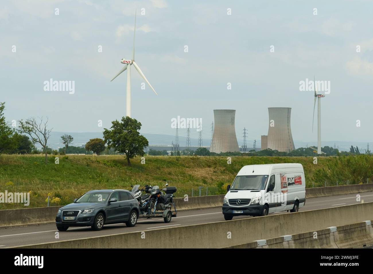 Lyon, France - May 16, 2023:A white van traveling down a highway alongside a massive wind turbine. The van is in motion, passing by the towering turbi Stock Photo