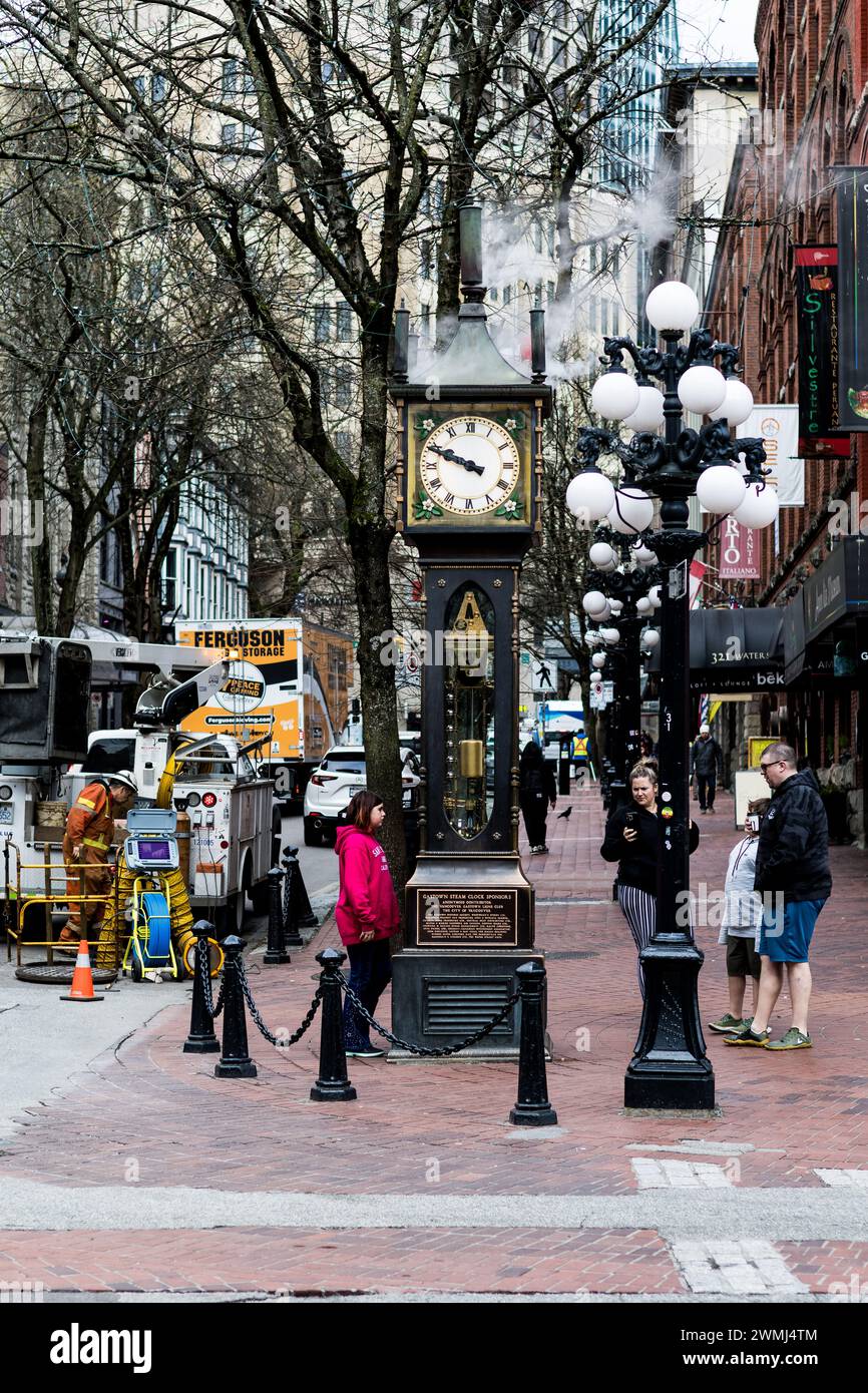 A view of the Steam Clock in Gastown, with steam coming out of its top and the details of its face, and a family of tourists looking at it. Stock Photo