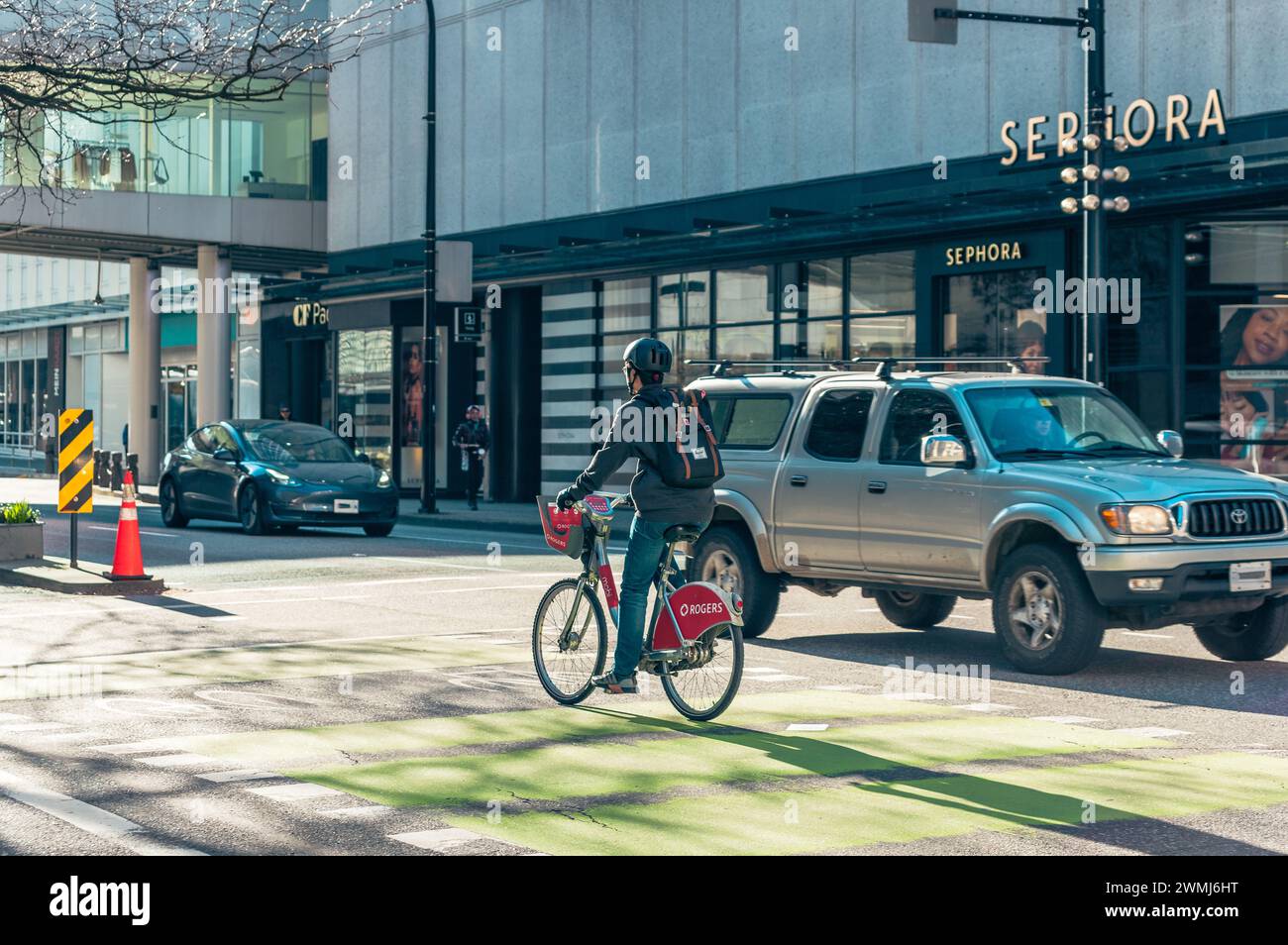 Vancouver, Canada - Feb 16 2024: A man riding his bike rental bicycle, using the bike lane on Dunsmuir Street, with cars driving beside him. Stock Photo