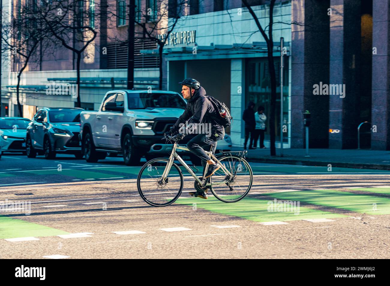 Vancouver, Canada - Feb 16 2024: A man riding his bicycle and crossing Dunsmuir Street on the bike lane, with cars stopped at the traffic light. Stock Photo