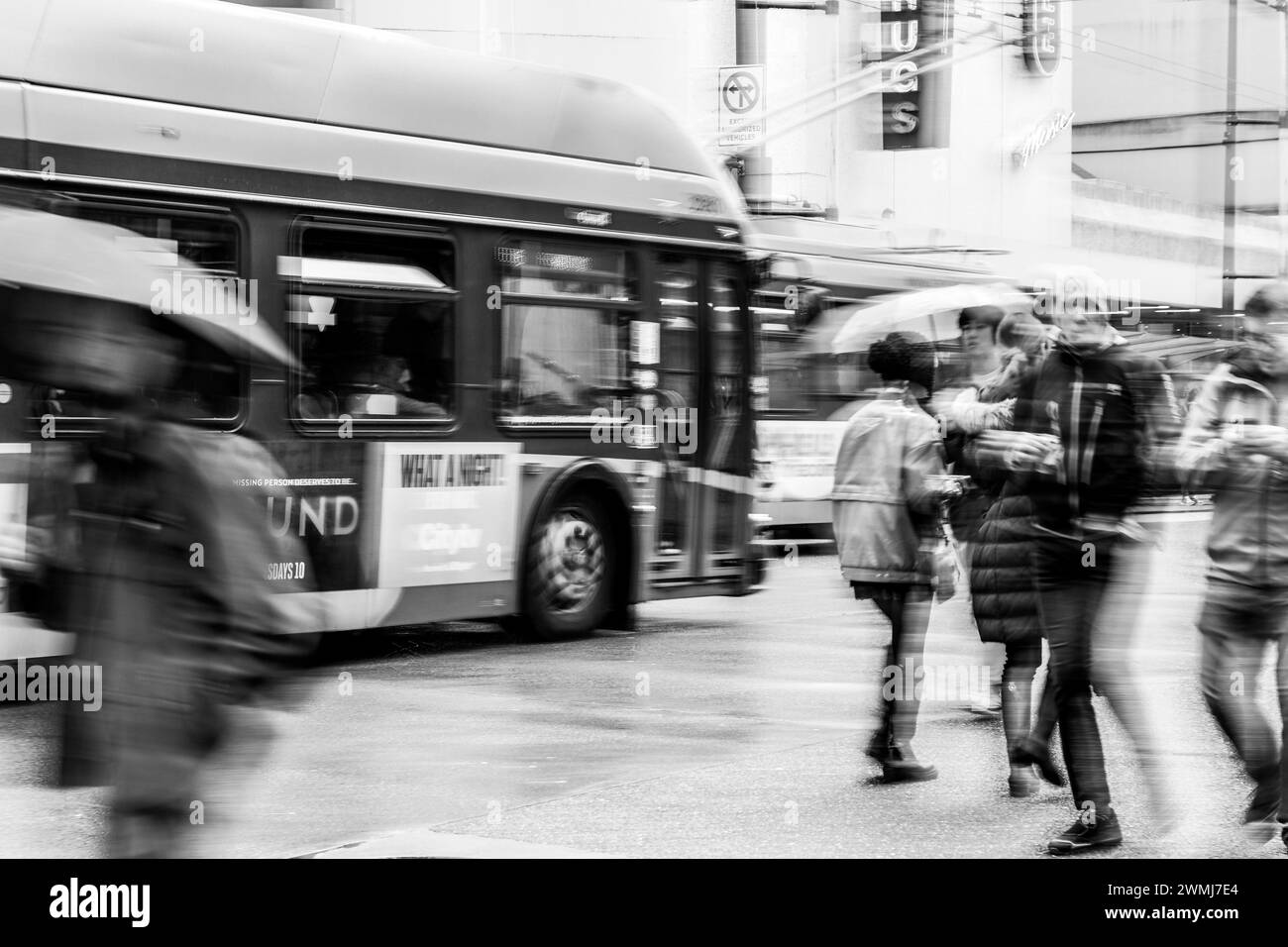 Vancouver, Canada - Feb 21 2024: A black and white scene of a bus and people crossing Georgia Street. The slow shutter speed has blurred their motion. Stock Photo