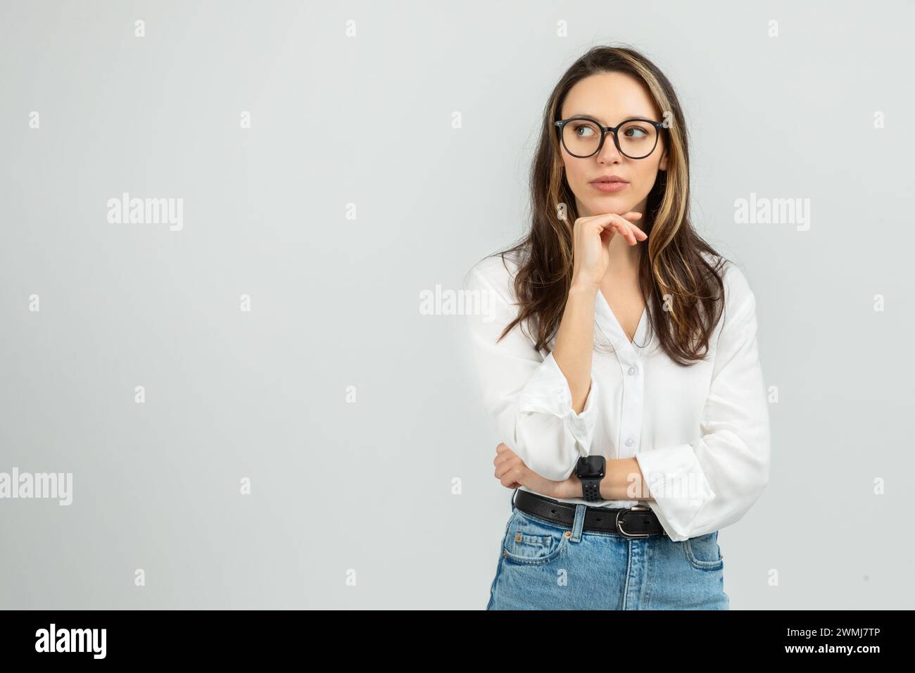 A contemplative young woman with long hair and glasses rests her chin ...