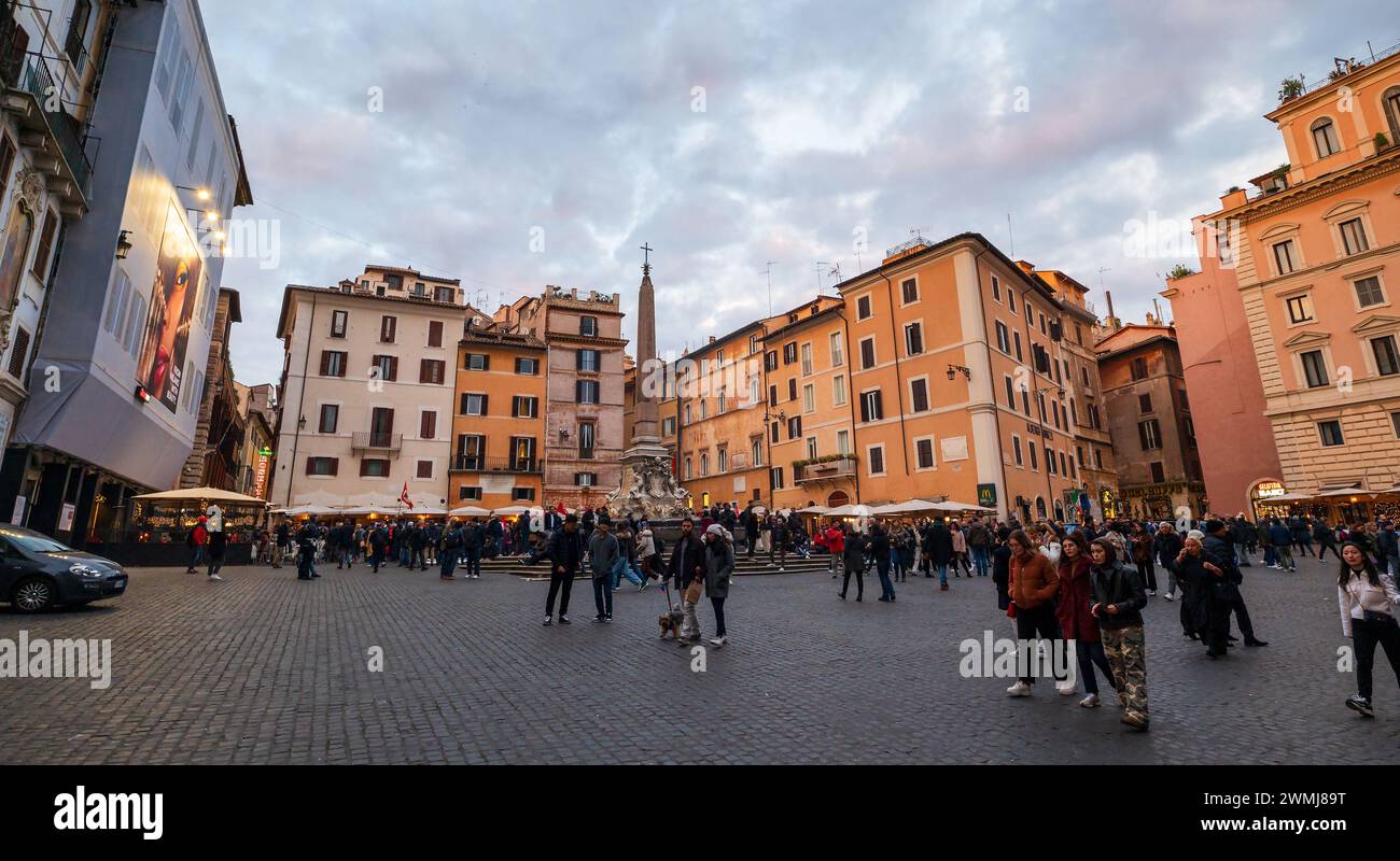 Rome, Italy - December 22, 2022: Wide-angle shot captures the vibrant atmosphere of a busy piazza surrounded by classical European buildings at dusk Stock Photo