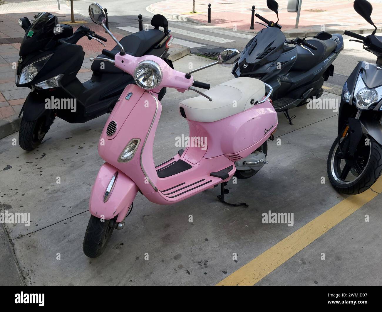 Pink Vespa 50 LX and other scooters parked on the street. Stock Photo