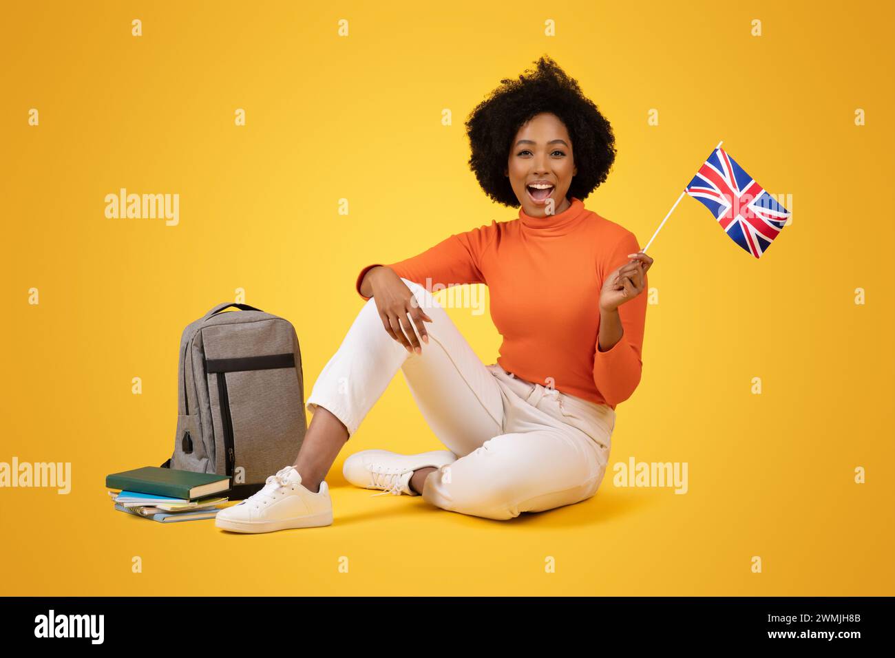 Excited African American woman sitting on the ground, holding a British flag with a joyful expression Stock Photo