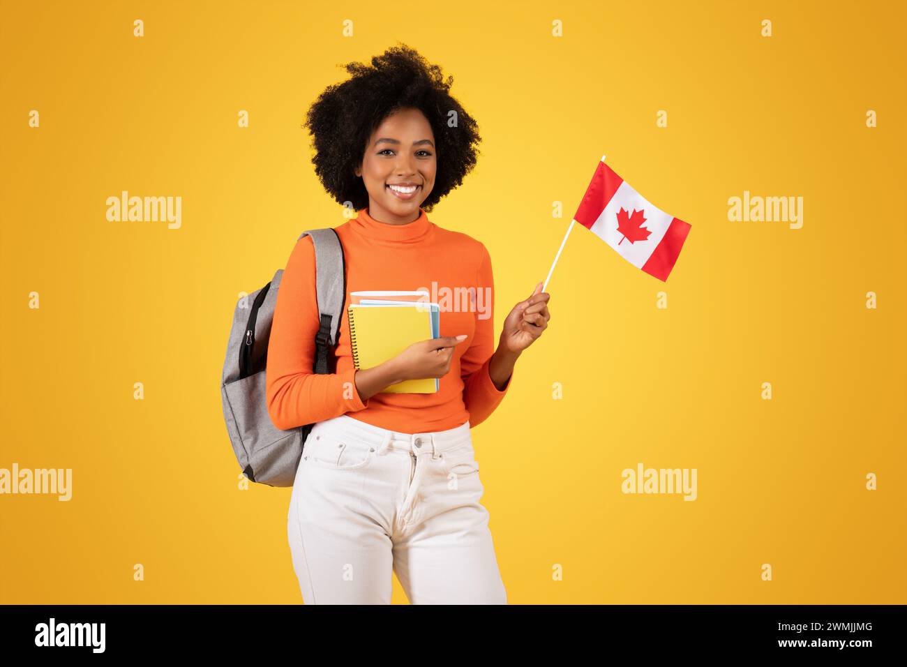 Smiling young woman with afro hair, dressed in an orange sweater and white jeans Stock Photo