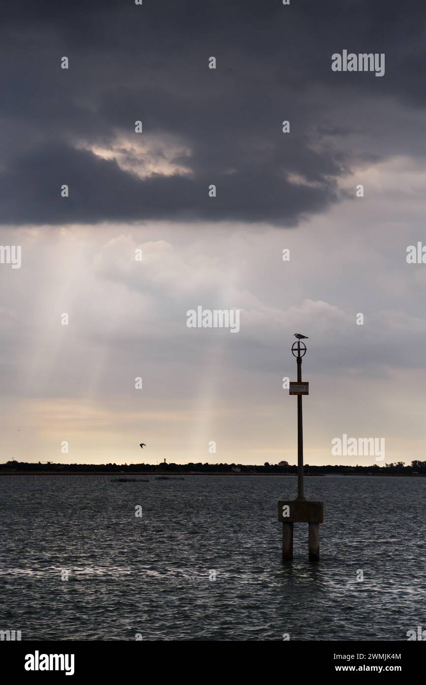 Waterway marker and uninhabited islands of Venetian lagoon with dark stormy sky in background. View from Burano island, Venice, Italy. Stock Photo