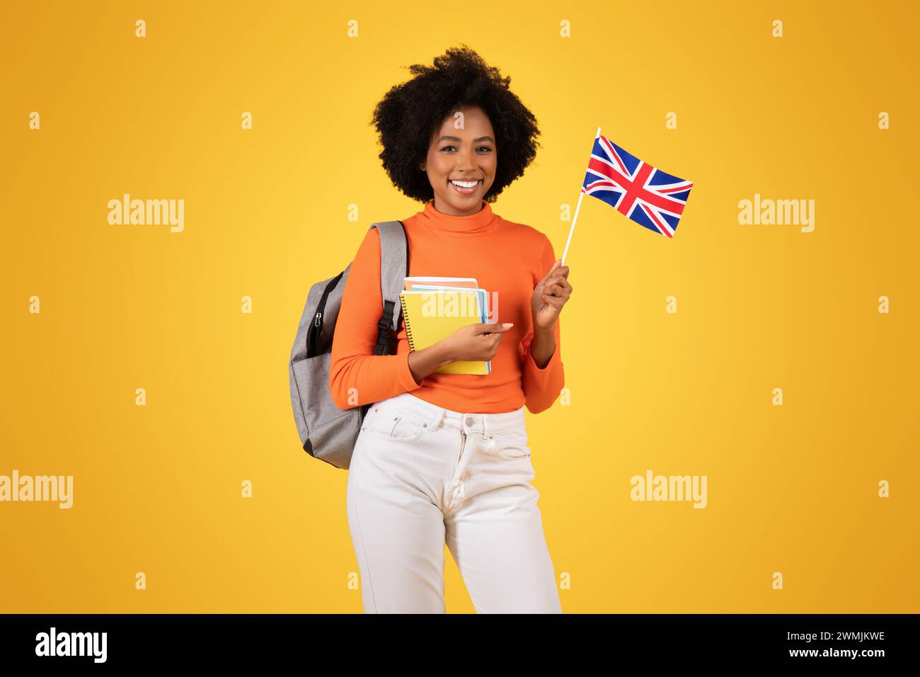 Smiling young student proudly holding a British flag, with notebooks and a gray backpack Stock Photo