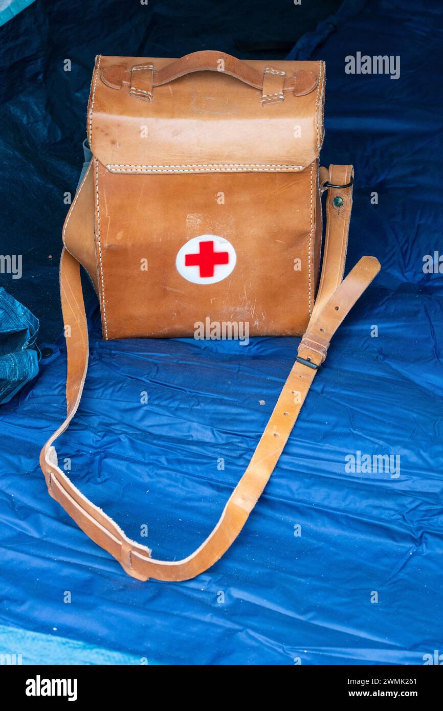 Vintage survival. Brown leather first aid bag with strap and red cross on white round shape. Inside blue scout tent. Stock Photo