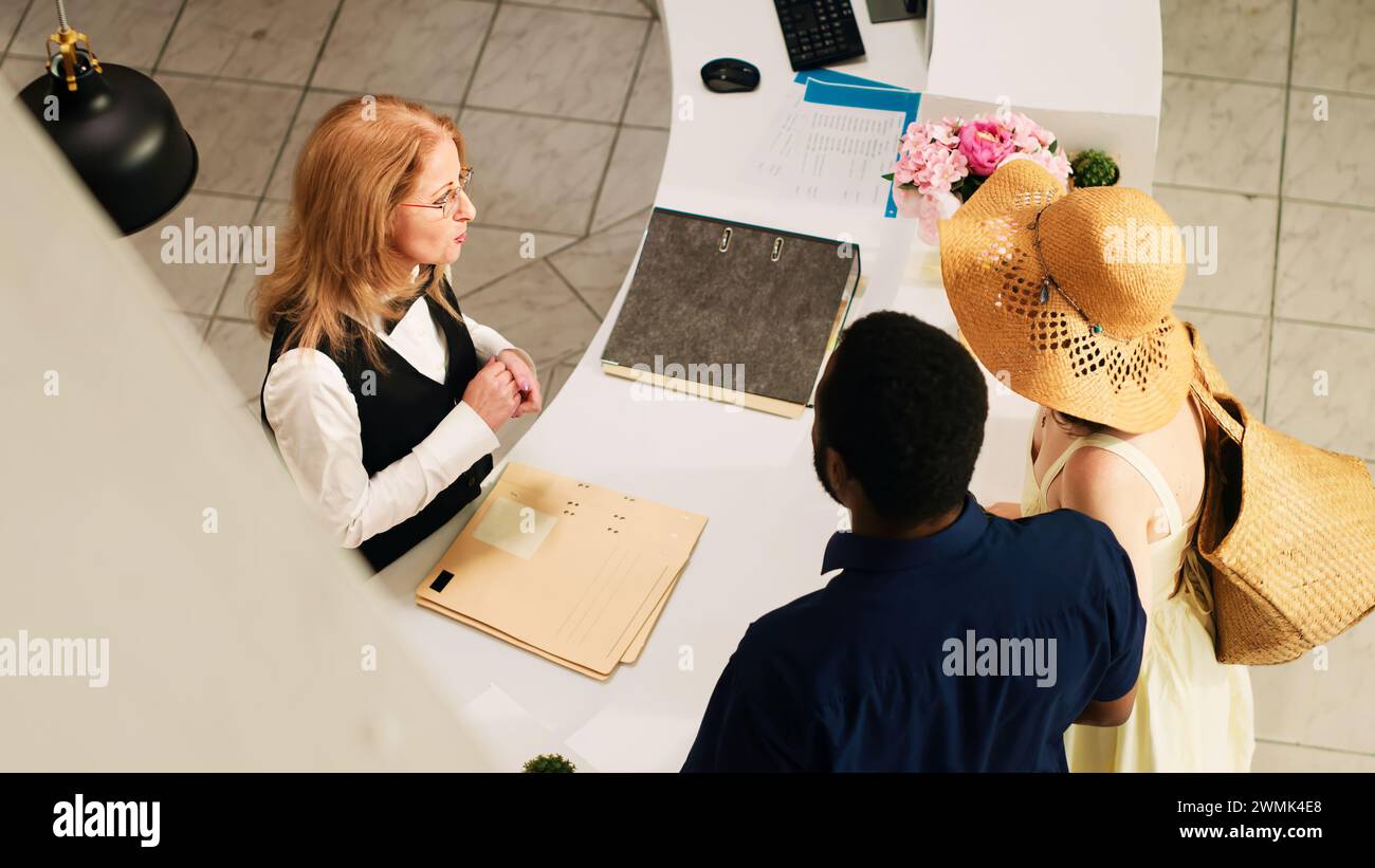 Receptionist doing check in process with hotel guests, couple on ...