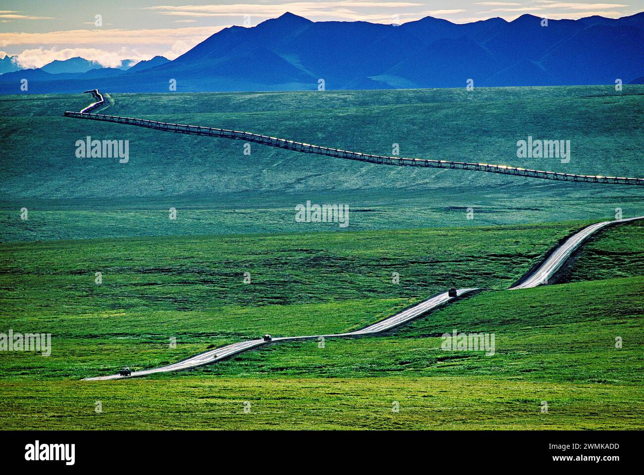 Three vehicles on the Dalton Highway, traverse rolling hills over the green tundra in summer, following the Trans-Alaska Pipeline in the background... Stock Photo