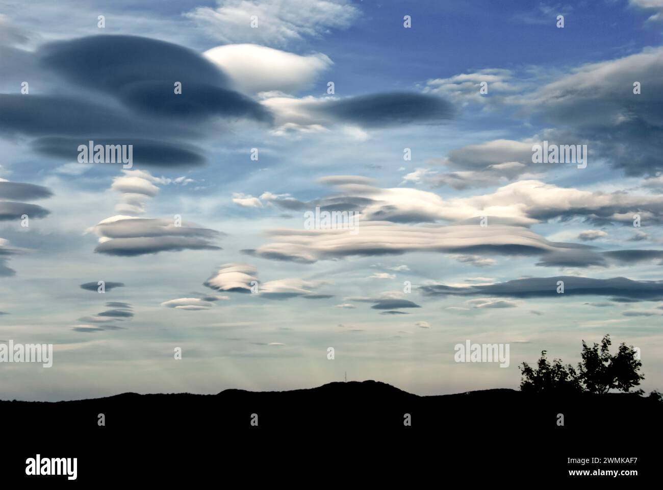 Lenticular clouds form over mountains. Anticrepuscular rays rise up to meet them. Stock Photo