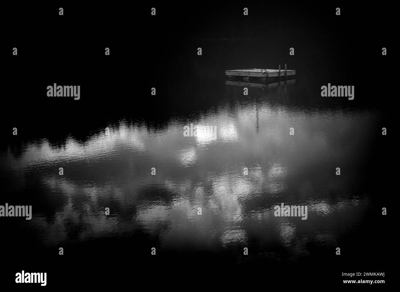 Black and white image of a dock floating on a tranquil lake Stock Photo